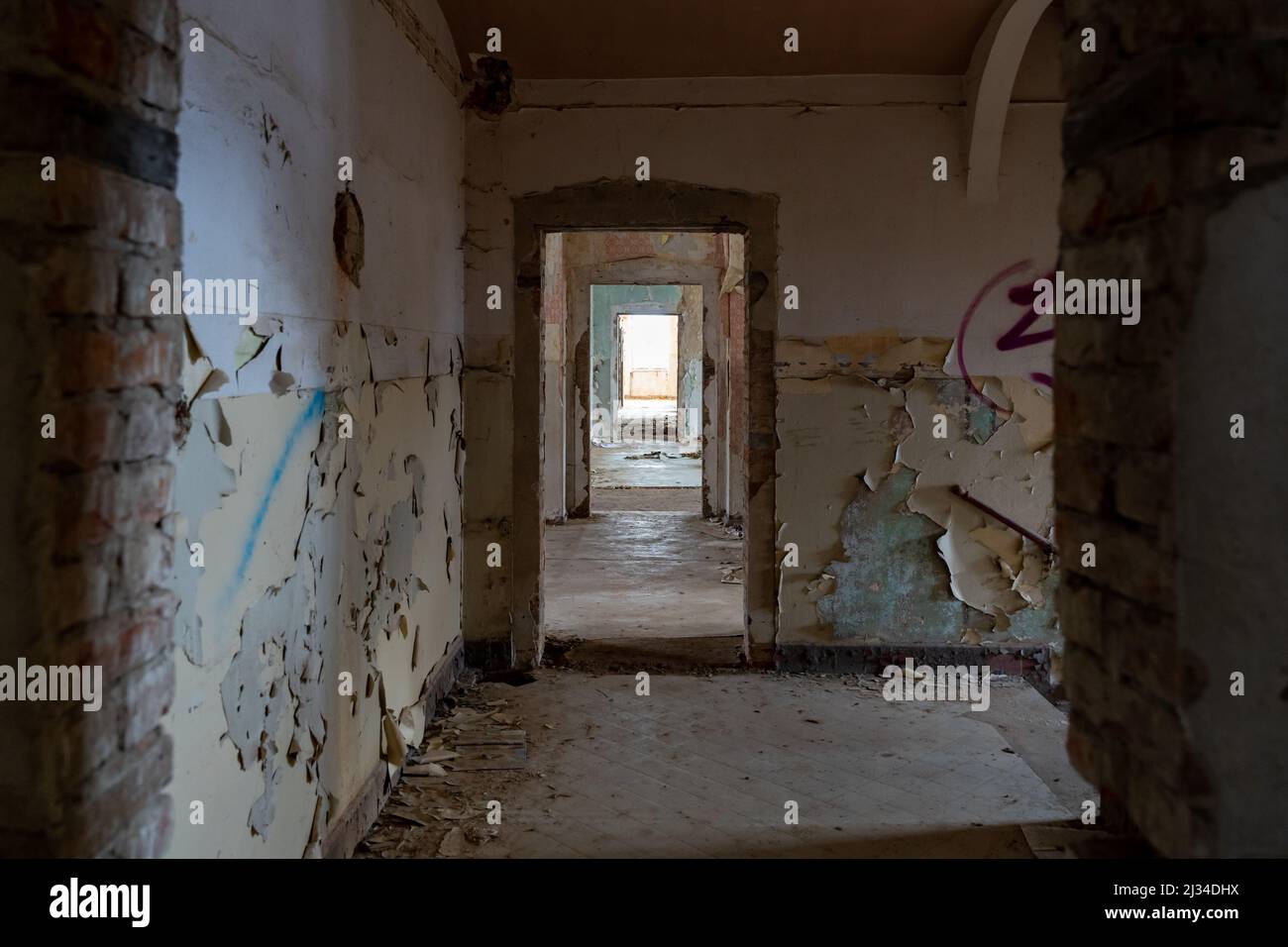 Dunkler Korridor in einem verlassenen öffentlichen Gebäude neben der Treppe. Urbane Erkundung in einem alten Horrorhaus. Die Farbe blättert von den schmutzigen Wänden ab. Stockfoto