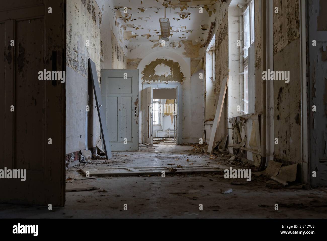 Langer und dunkler Korridor in einem verlassenen öffentlichen Gebäude mit vielen Holztüren. Urbane Erkundung in einem großen alten Haus. Die Farbe blättert ab. Stockfoto