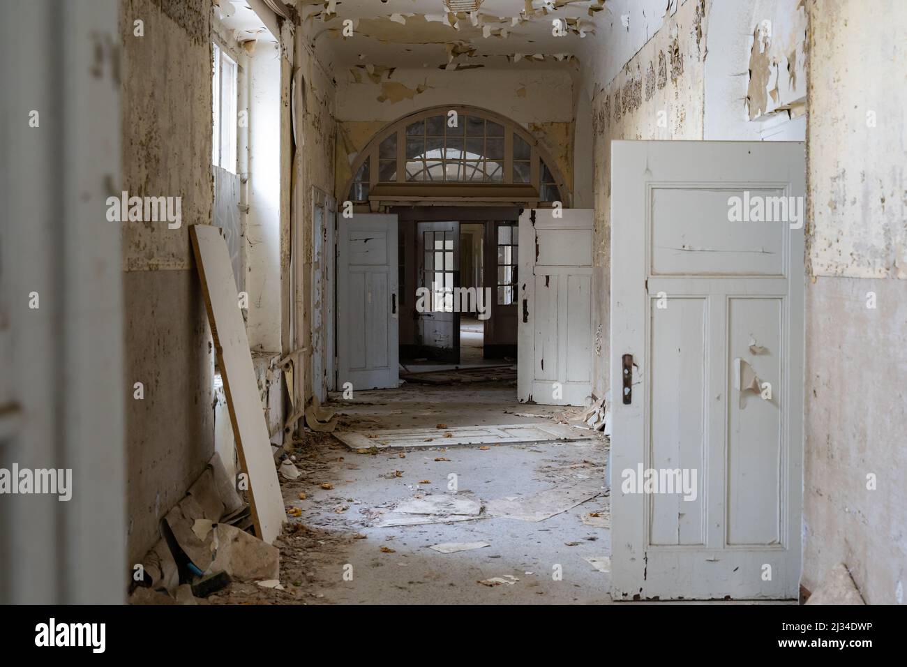 Langer Korridor in einem verlassenen öffentlichen Gebäude mit vielen Holztüren. Urbane Erkundung in einem großen alten Haus. Die Farbe blättert von den Wänden. Stockfoto