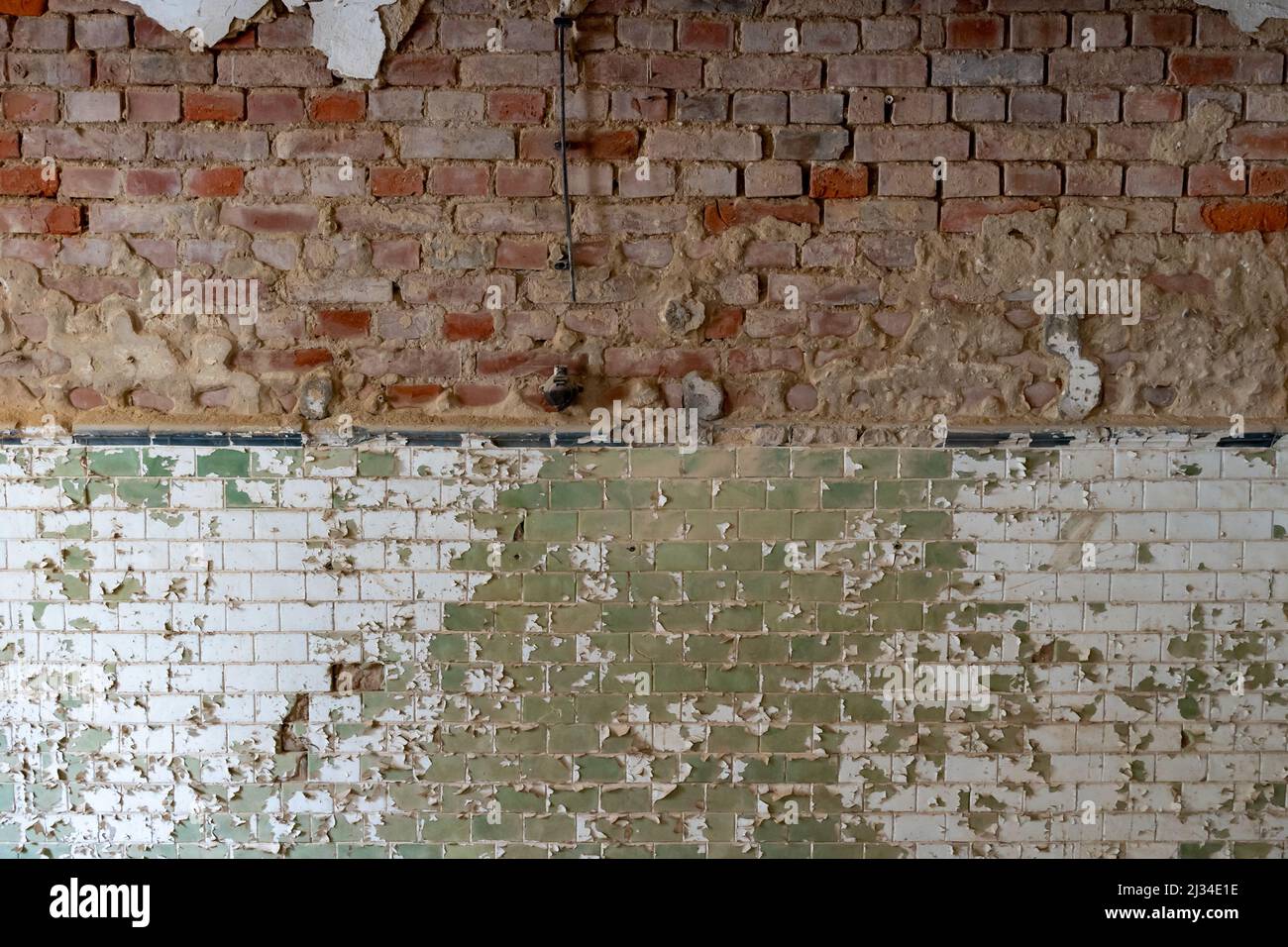 Verwitterte alte Steinmauer mit roten Ziegeln und grünen Fliesen. Die Farbe blättert vom Gebäude ab. Hintergrundtextur einer schmutzigen realen Oberfläche. Beschädigte Ruine Stockfoto