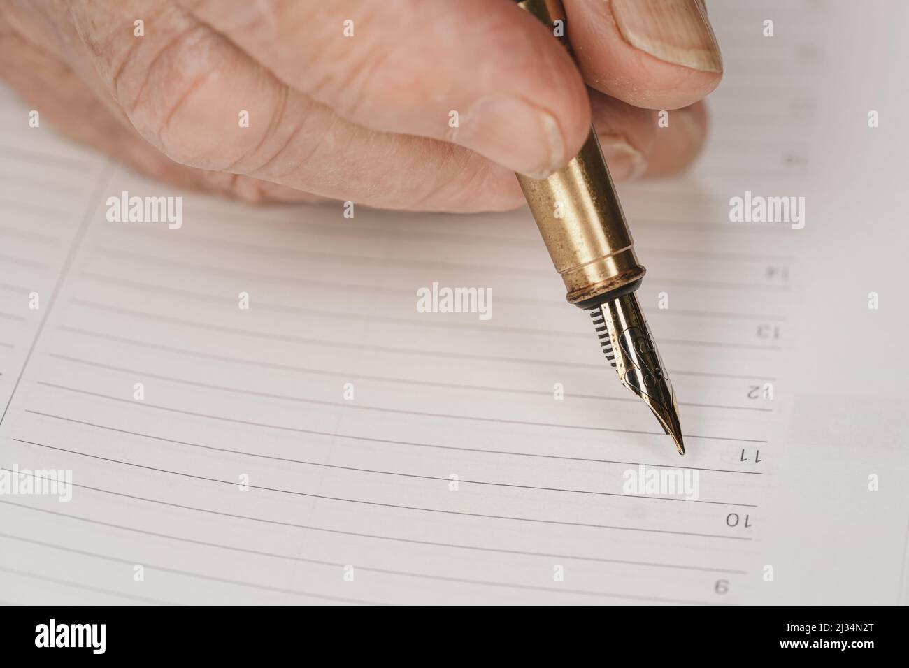 Goldfarbene Fontäne Tinte Stift in Senior Frau Hand über etwas auf leere tägliche Planer Seite schreiben, Nahaufnahme Detail Stockfoto