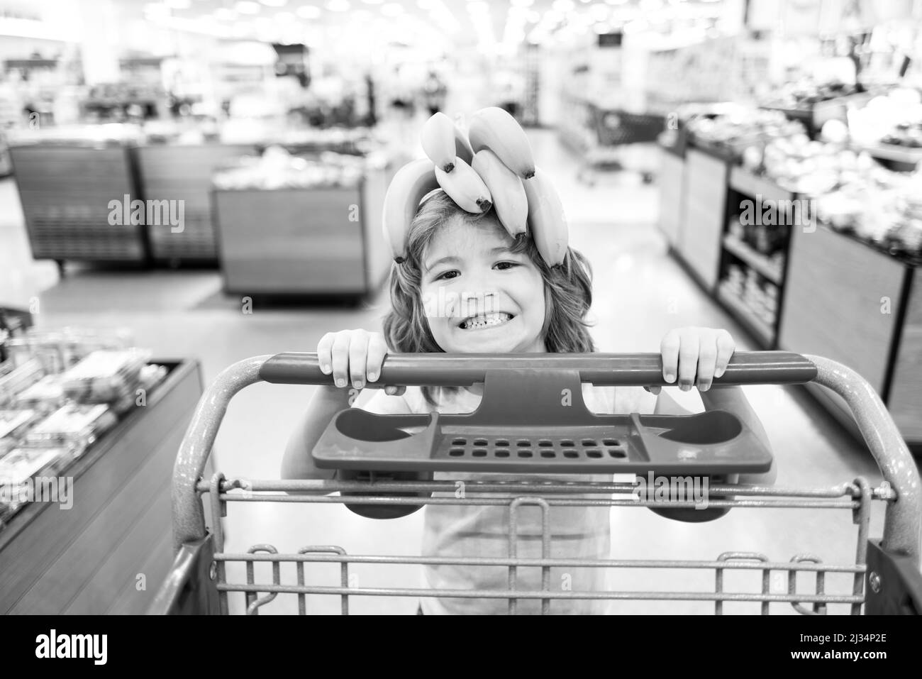 Kind mit Einkaufswagen im Supermarkt oder Supermarkt. Kind kauft Bananenfrüchte auf dem Lebensmittelmarkt. Stockfoto