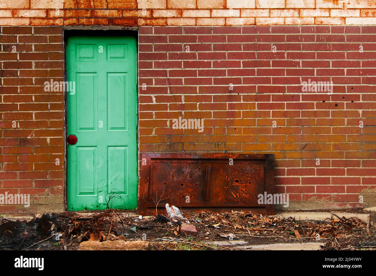 Eine grüne alte Vintage-Tür Stahl roten Backstein Gasse Wand rostigen Schutt Lagerhaus Fabrik Versand Eingang Hintertür Mitarbeiter Eingang Stockfoto