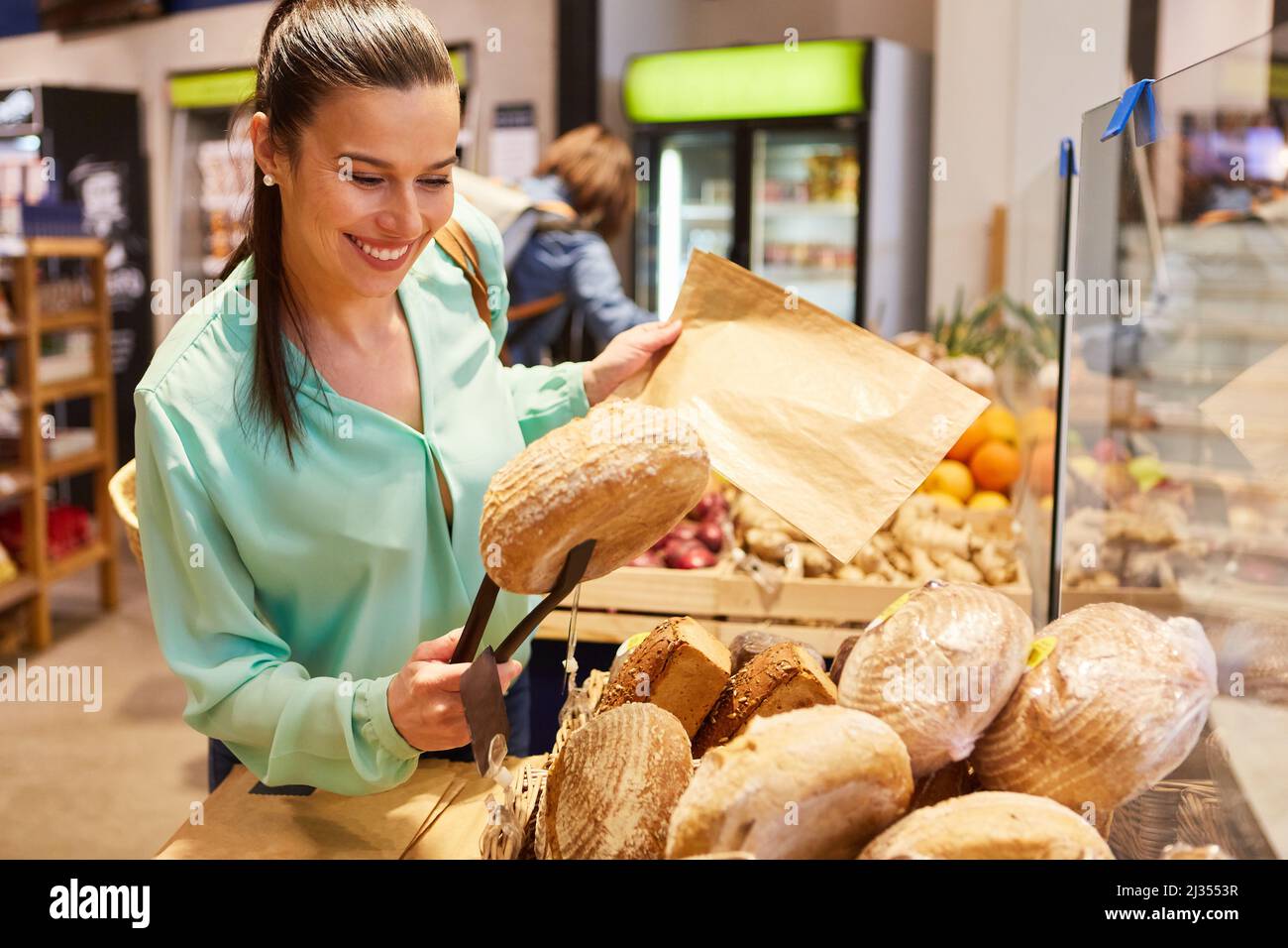 Junge Frau als glückliche Kundin, die Brot als Selbstbedienung im Supermarkt kauft Stockfoto