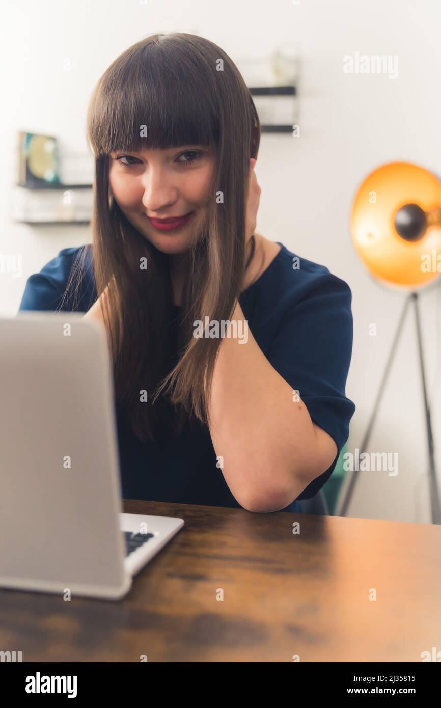 Schöne junge europäische Frau, die zu Hause arbeitet, auf die Kamera schaut und lächelt, am Holztisch sitzt Remote Job Concept Copy Space. Hochwertige Fotos Stockfoto