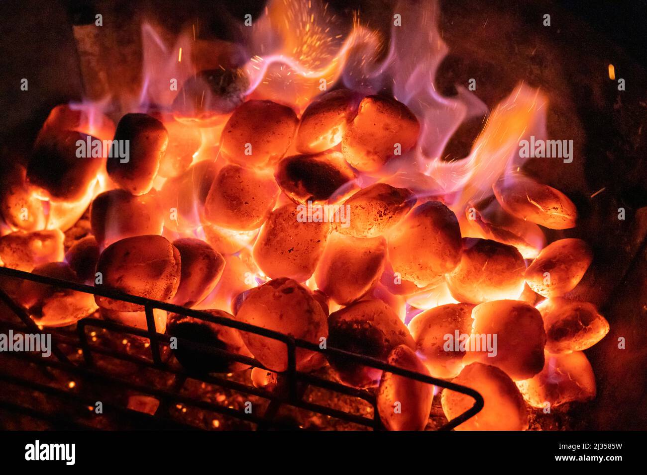 Heiße Kohlen auf einem Grill in der Nacht mit einer Grillvorführen. Konzept: Grillen, Grillen, grillen, Wärme, Grillen, Heiße Kohlen, brennende Kohlen, Hitze, Brennstoff Stockfoto