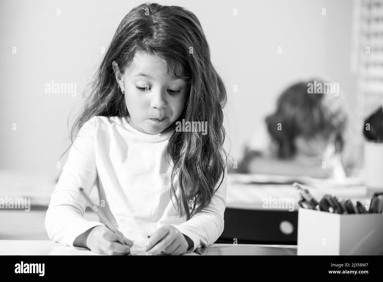 Lustige Schüler im Klassenzimmer in der Schule. Kleines Mädchen, das im Unterricht am Schreibtisch sitzt. Portrait der jungen Schülerin studieren und schreiben auf Notebook. Konzentriert Stockfoto