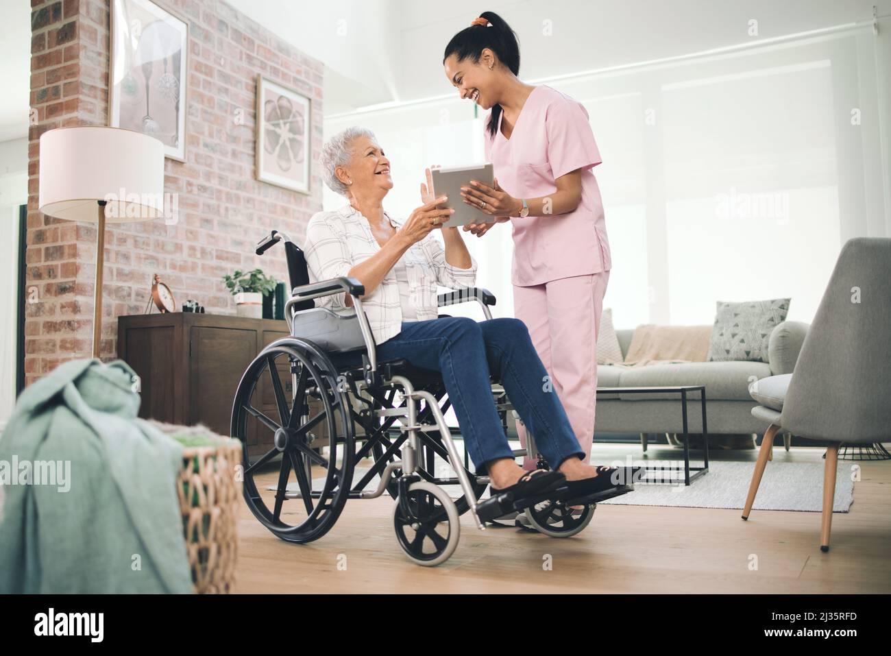 Ich habe all Ihre großen Momente festgehalten. Aufnahme einer jungen Krankenschwester, die Informationen von ihrem digitalen Tablet mit einer älteren Frau im Rollstuhl teilt. Stockfoto