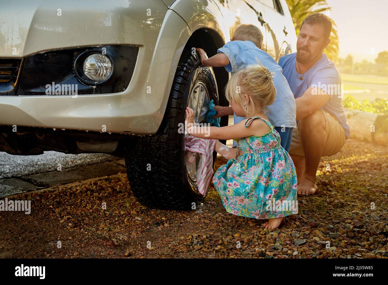 Sie sind immer bestrebt, Papa beim Waschen des Autos zu helfen. Aufnahme einer Familie, die ihr Auto gemeinsam wäscht. Stockfoto