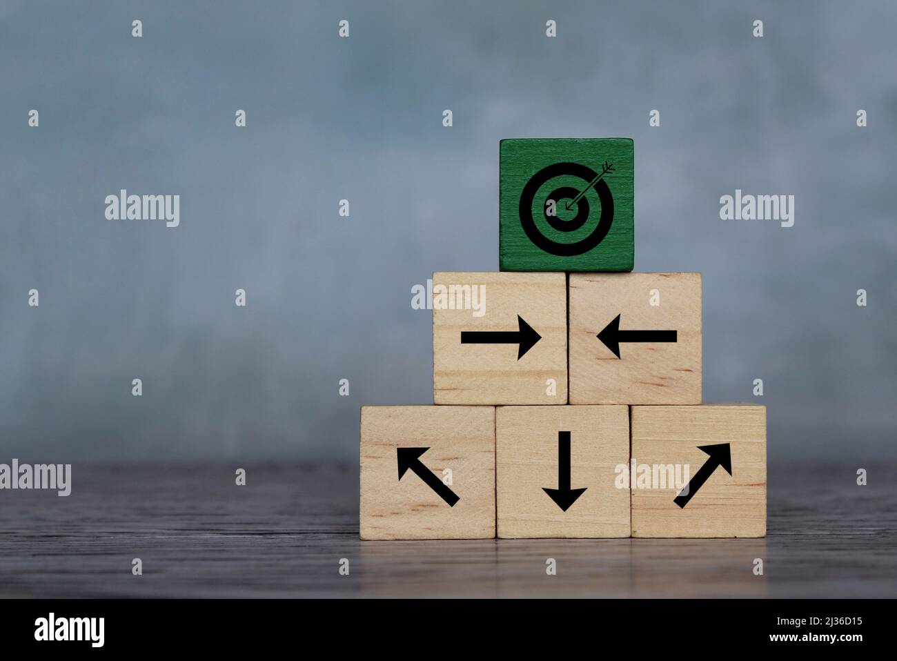 Holzwürfel mit Zielsymbol und Pfeil, der in eine andere Richtung zeigt. Organisieren Sie ein Team, setzen Sie ein Ziel. Stockfoto
