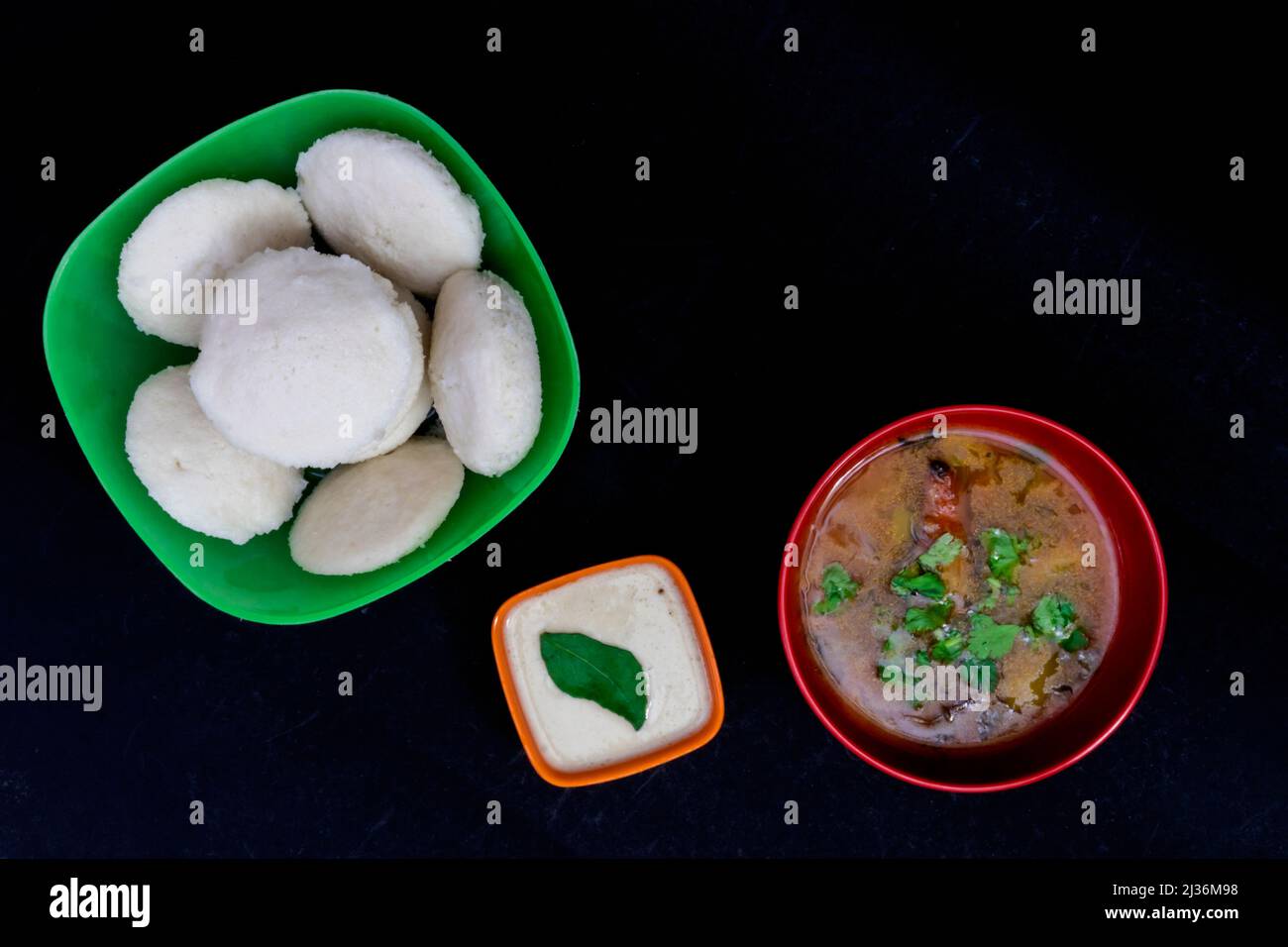 Untätig Sambar mit Coconut Chutney, isoliert auf schwarzem Hintergrund, südindisches Frühstück, untätig in grüner quadratischer Schüssel, Sambar in roter runder Schüssel, Coconut C Stockfoto