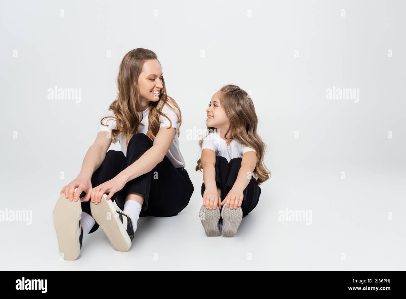 Mutter und Tochter in schwarz-weißen Kleidern lächeln einander an, während sie auf grauem Hintergrund sitzen Stockfoto