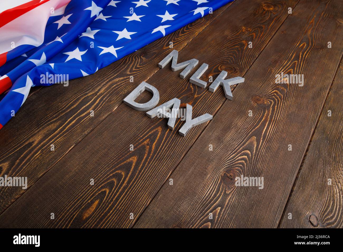 Das Wort MLK Day lag mit silbernen Metallbuchstaben auf einer hölzernen Oberfläche mit zerknitterter US-Flagge auf der linken Seite. MLK bedeutet Martin Luther King Jr. Stockfoto