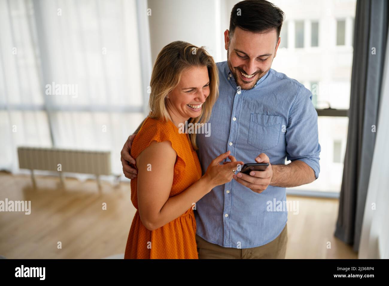 Lächelndes Paar, das sich mit einem Smartphone umarmt. Menschen, die soziale Medien auf dem Mobiltelefon teilen. Stockfoto