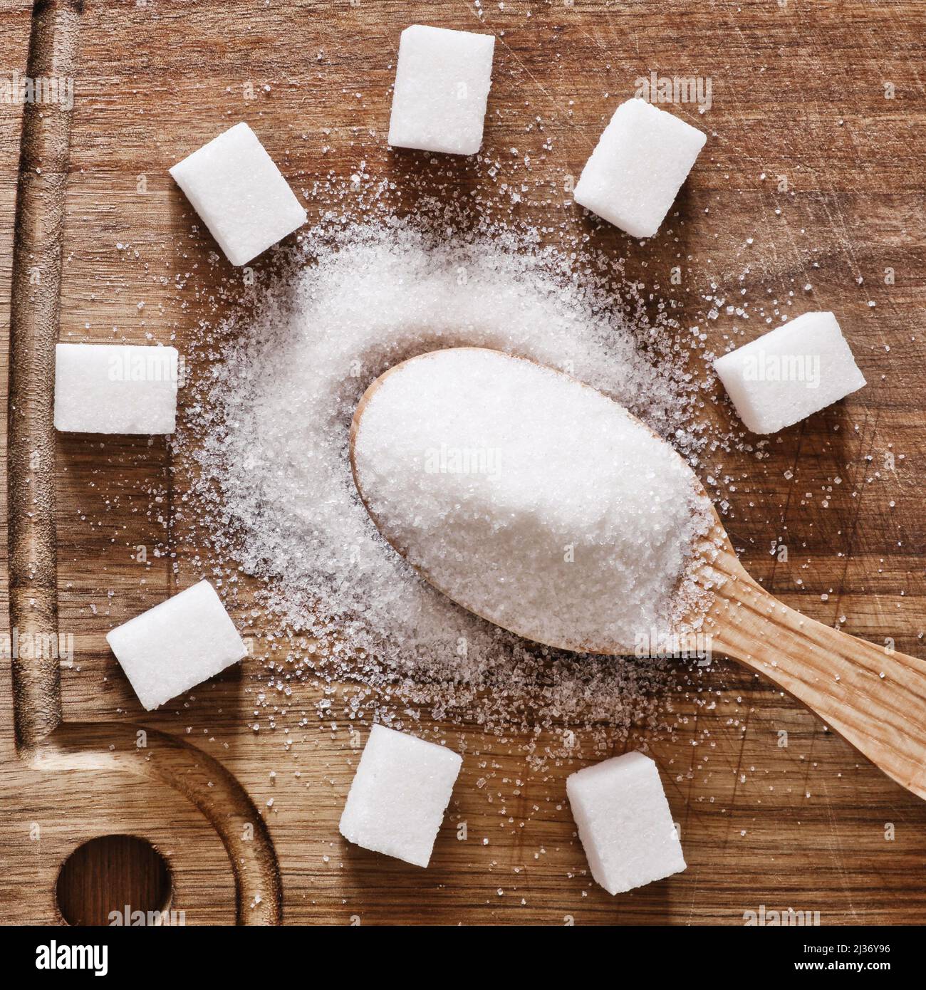 Der Holzlöffel voll mit Granulatzucker und Zuckerwürfeln auf Holzgrund herum. Stockfoto