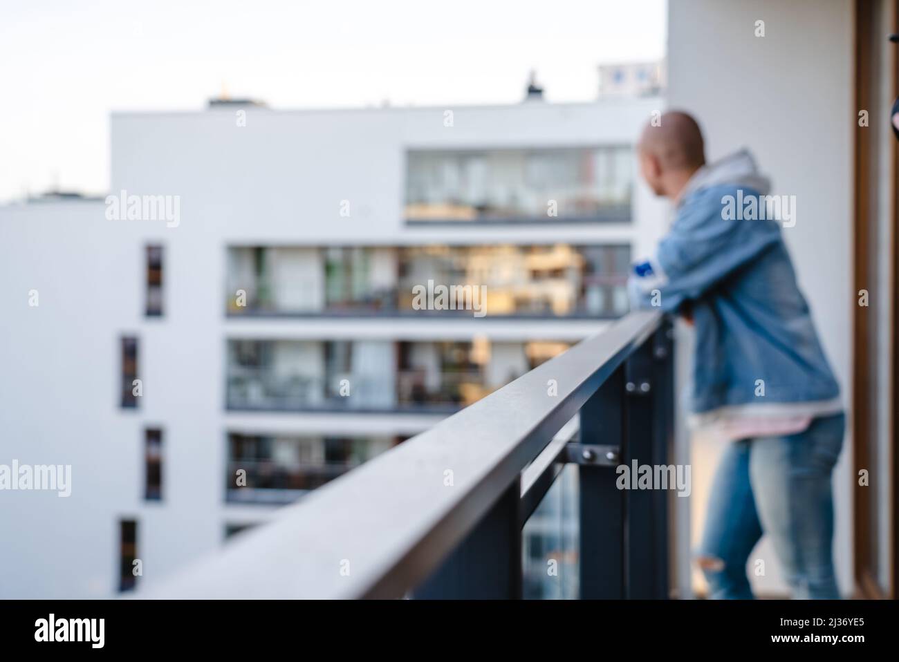 Verschwommenes Foto einer jungen Glatze, die auf dem Balkon stand, ihre Arme auf einer Leitplanke ausstreckte und die Nachbarschaft betrablickte. Hochwertige Fotos Stockfoto