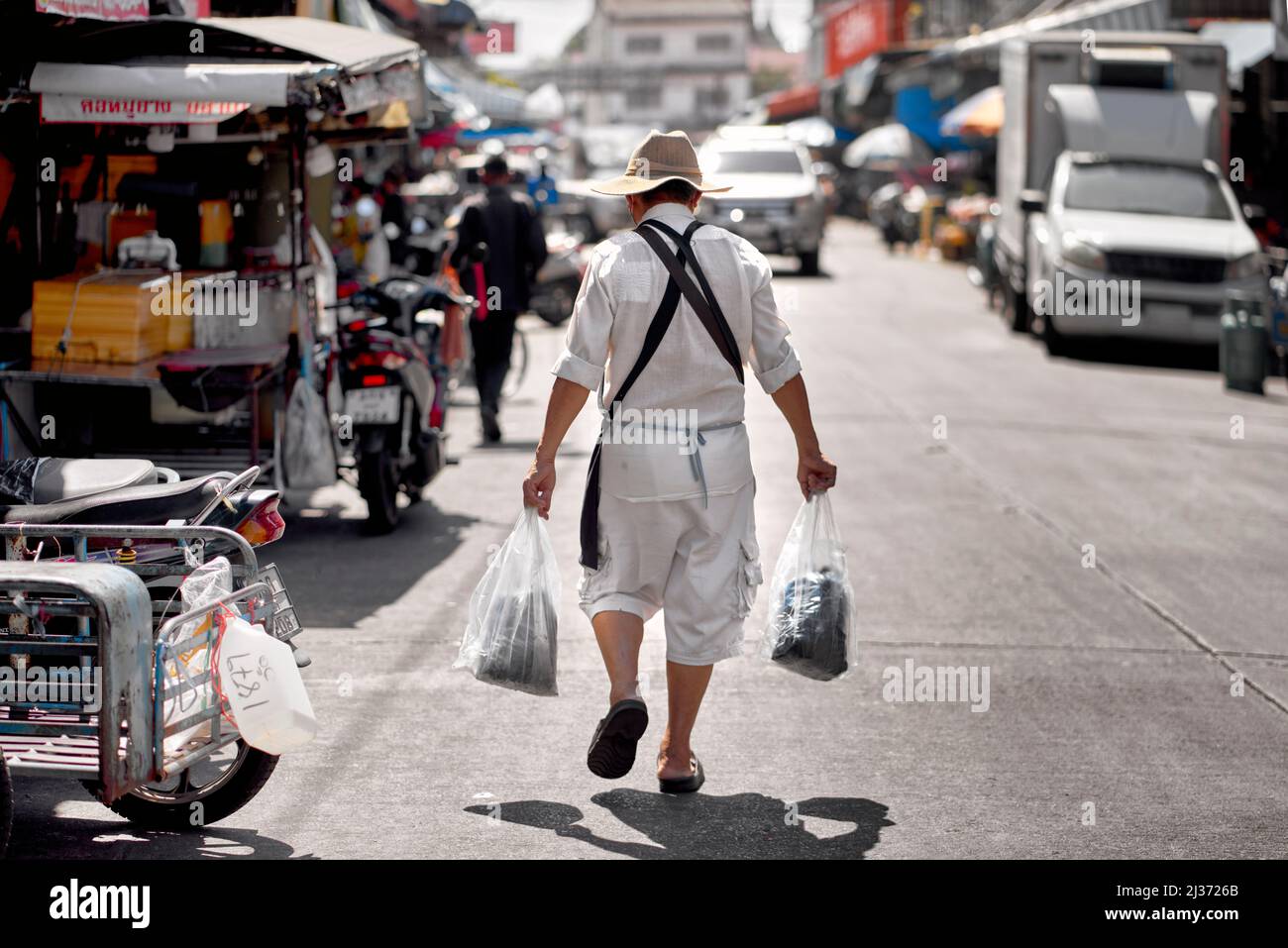 Mann, der auf dem thailändischen Straßenmarkt einkauft und Plastiktüten mit gekauften Waren trägt Stockfoto