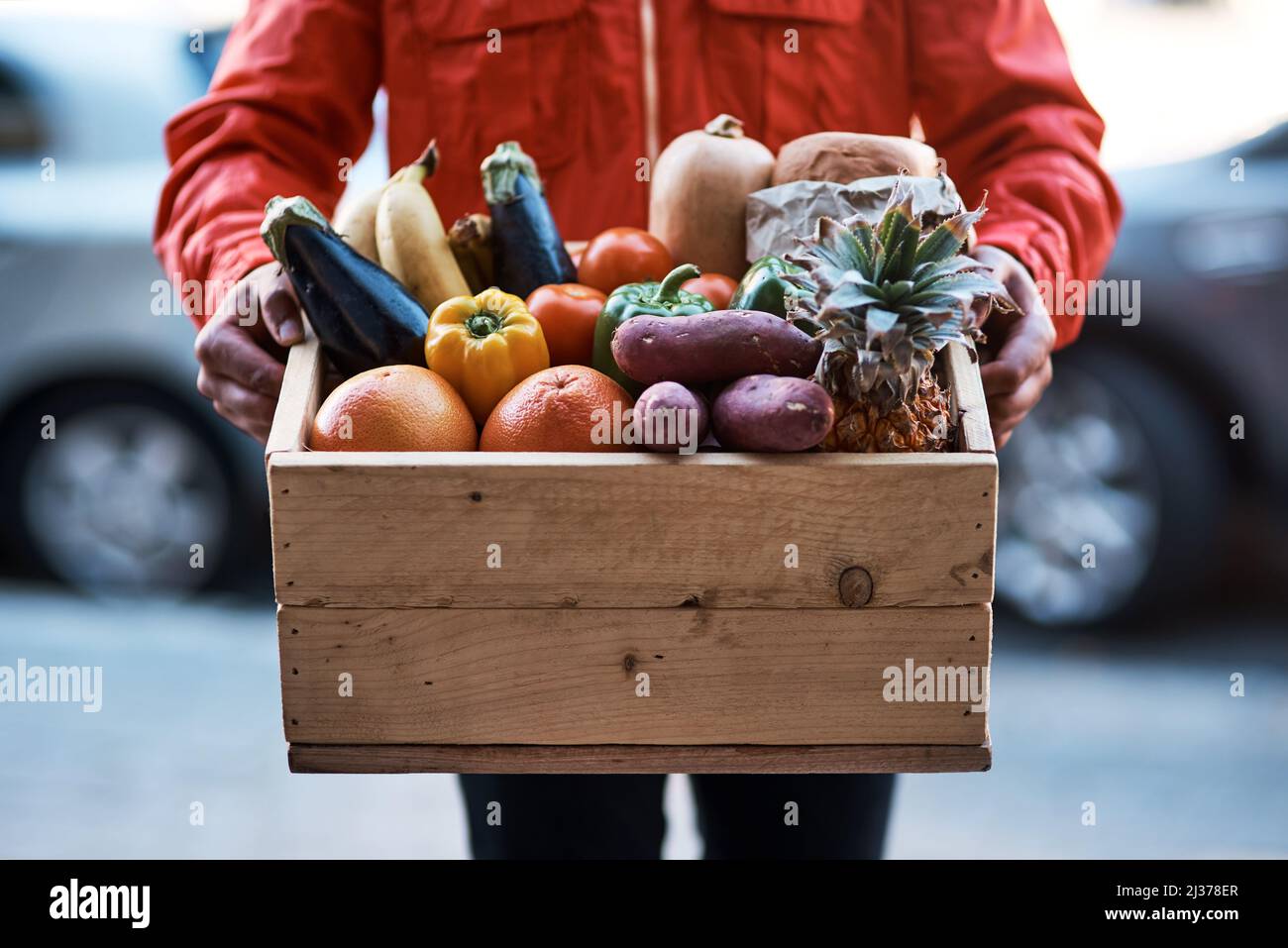 Frisch direkt vor die Tür geliefert. Kurzer Schuss eines Mannes, der eine Kiste voller Obst und Gemüse liefert. Stockfoto