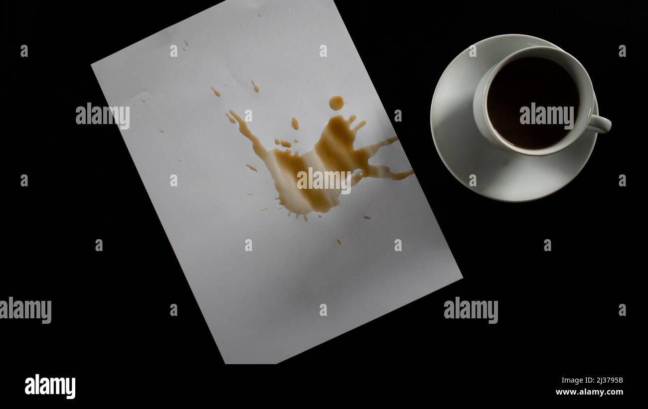 Papier mit verschüttetem Kaffee, Filterkaffee auf schwarzem Tisch, weiße Tasse und Untersetzer, isoliert auf schwarzem Hintergrund, Draufsicht Stockfoto