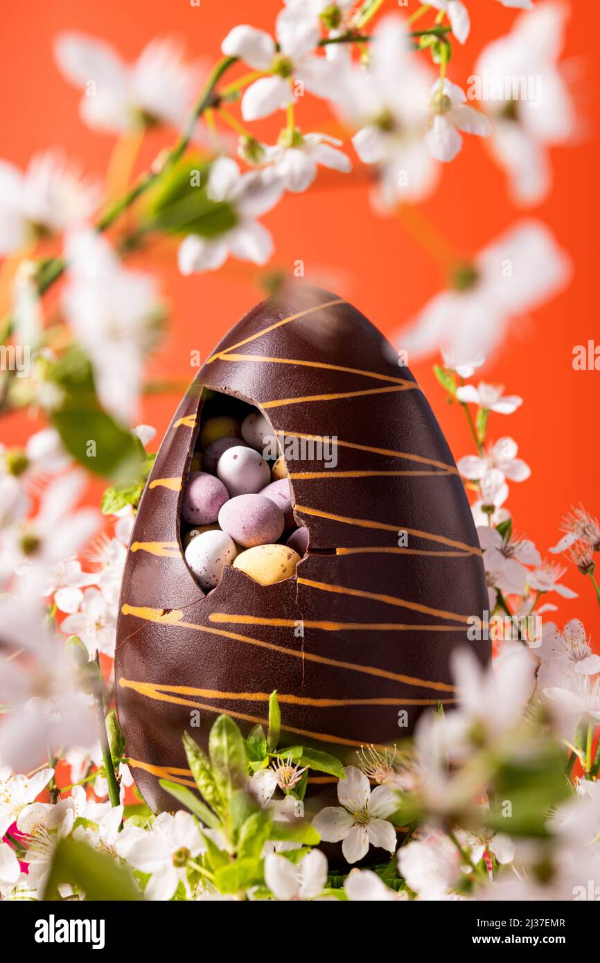 Osterschokoladenei mit Frühlingsblumen auf leuchtendem orangefarbenem Hintergrund Stockfoto