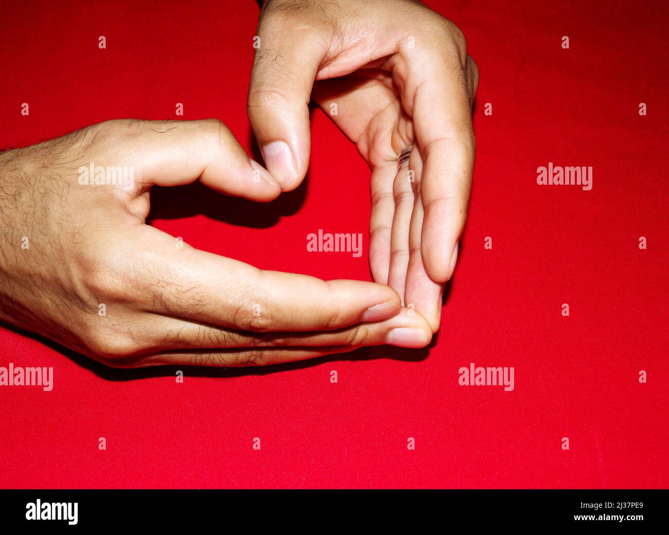 Herz, geformt durch die Hände eines erwachsenen Mannes mit markanten Schatten auf rotem Hintergrund Stockfoto