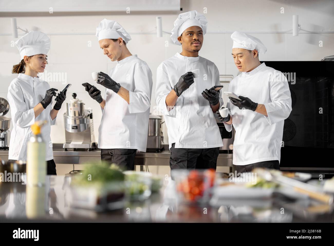 Team von multirassischen Köchen, die während einer Kaffeepause in der Küche ein Gespräch führen. Gut gekleidete Köche ruhen sich aus und haben Spaß in der Restaurantküche. Teamarbeit und Freizeit am Arbeitsplatz Stockfoto