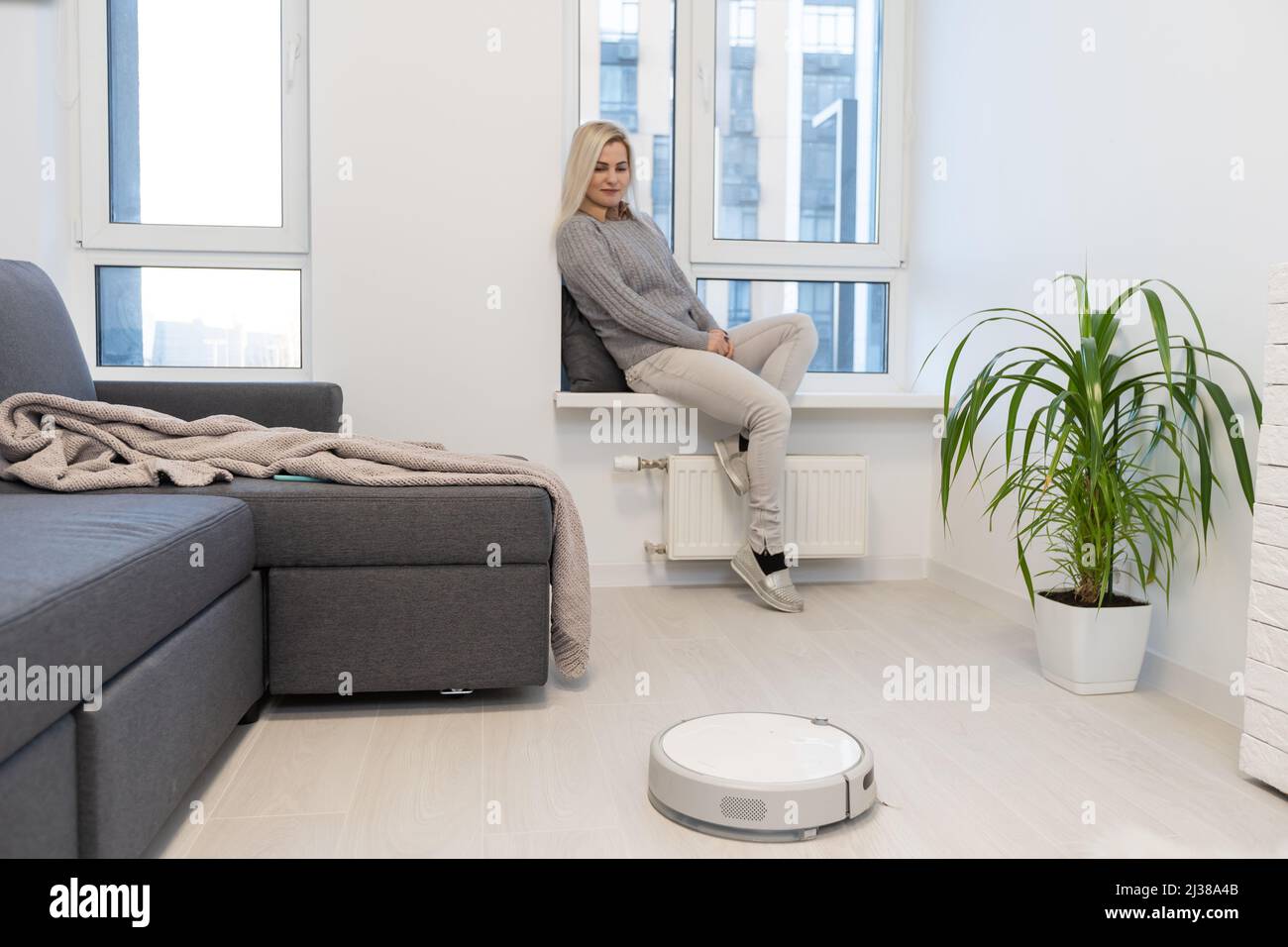 Roboter Staubsauger Reinigen der Zimmer, während Frau Entspannen auf dem Sofa. Frau controlling Vakuum mit Fernbedienung. Stockfoto