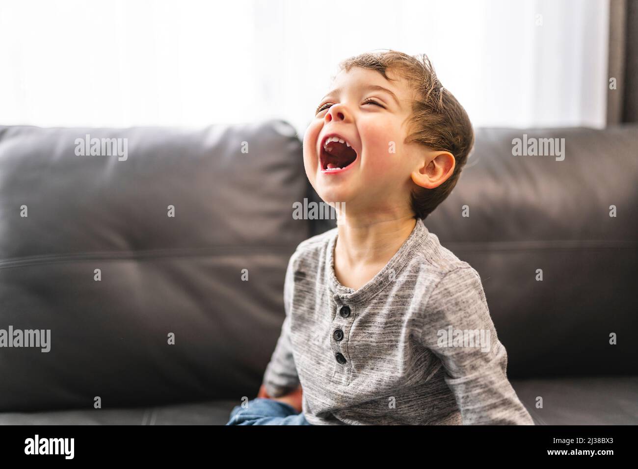 Der kleine Junge steht zu Hause mit einem großen Lachen auf dem Sofa Stockfoto