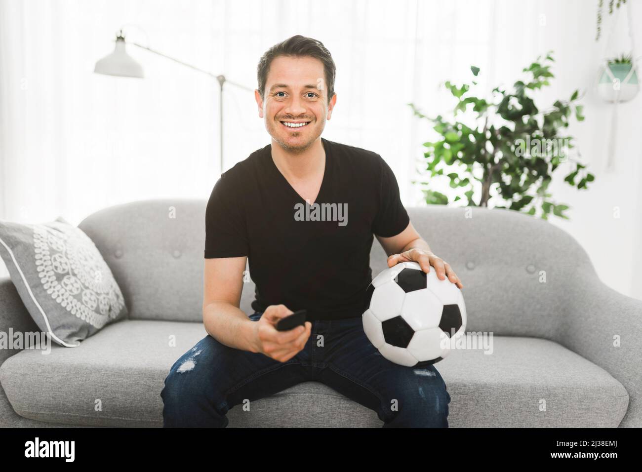 Porträt eines begeisterten Mannes, der im Fernsehen ein europäisches Fußballspiel ansieht und das Tor auf der Couch feiert Stockfoto