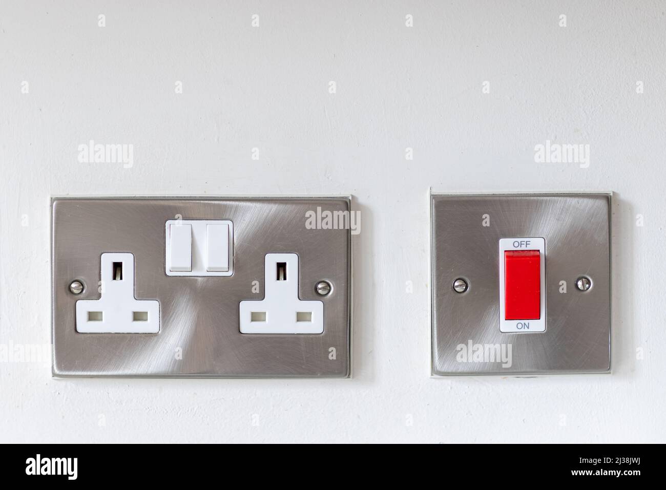 Elektrische Doppelsteckdose aus Edelstahl und roter ein-/Ausschalter an einer weißen Wand Stockfoto