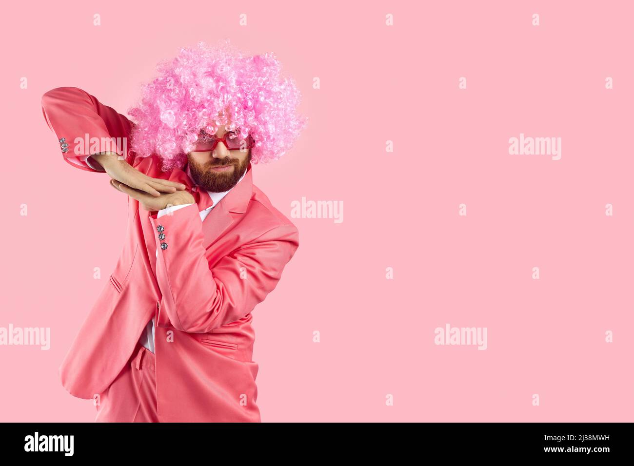 Lustiger Mann in pinkem Partyanzug, Clown Perücke und funky Brille tanzen auf pinkem Copy Space Hintergrund Stockfoto