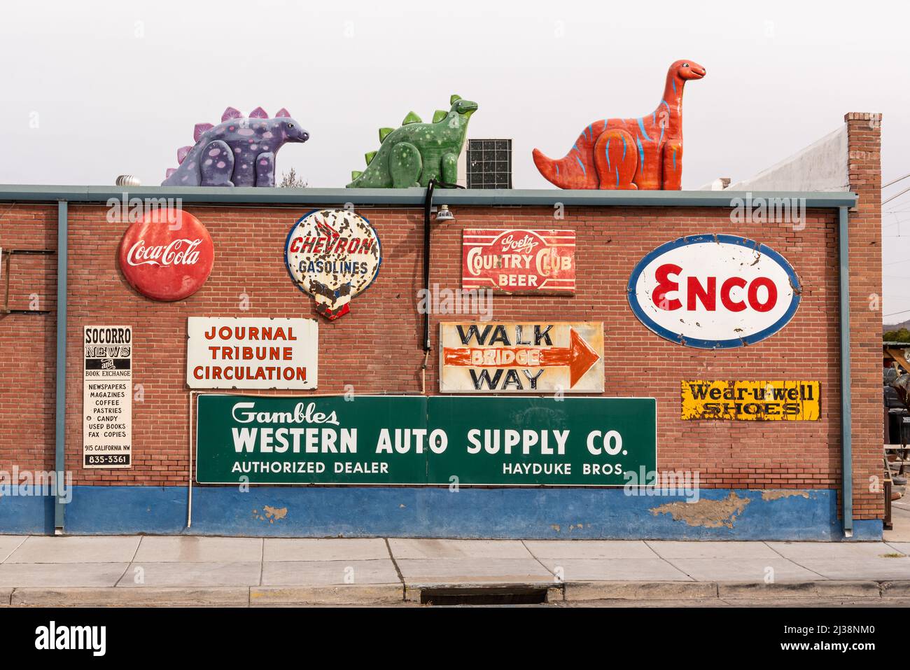 Vintage-Schilder an einer roten Backsteinmauer und Dinosaurier auf dem Dach von Sparky's, einem beliebten Restaurant und Straßenattraktion, und in Hatch, New Mexico. Stockfoto