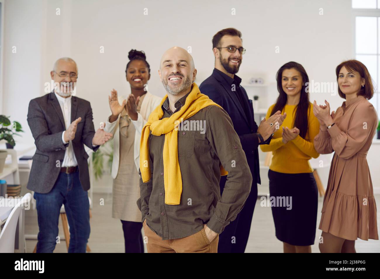 Glücklicher erfolgreicher Teamleiter, der vor seinen applaudierenden Mitarbeitern steht Stockfoto