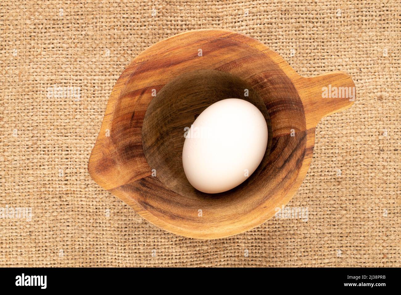 Ein Hühnereier in einem Holzbecher auf Sackleinen, Makro, Draufsicht. Stockfoto