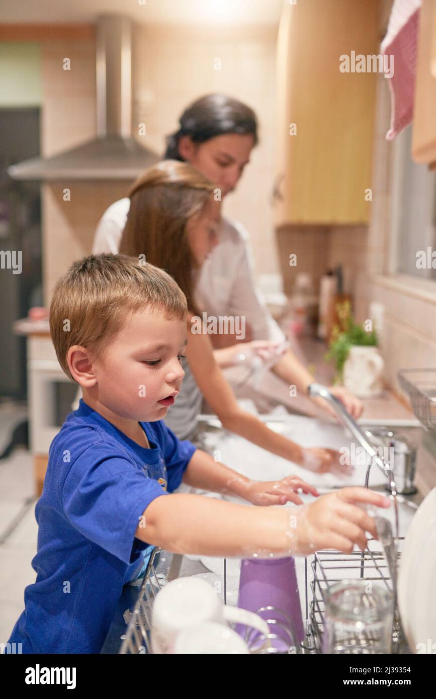 Viele Hände bei der Arbeit. Aufnahme eines kleinen Jungen, der mit seiner Familie an einem Spülbecken abspült. Stockfoto