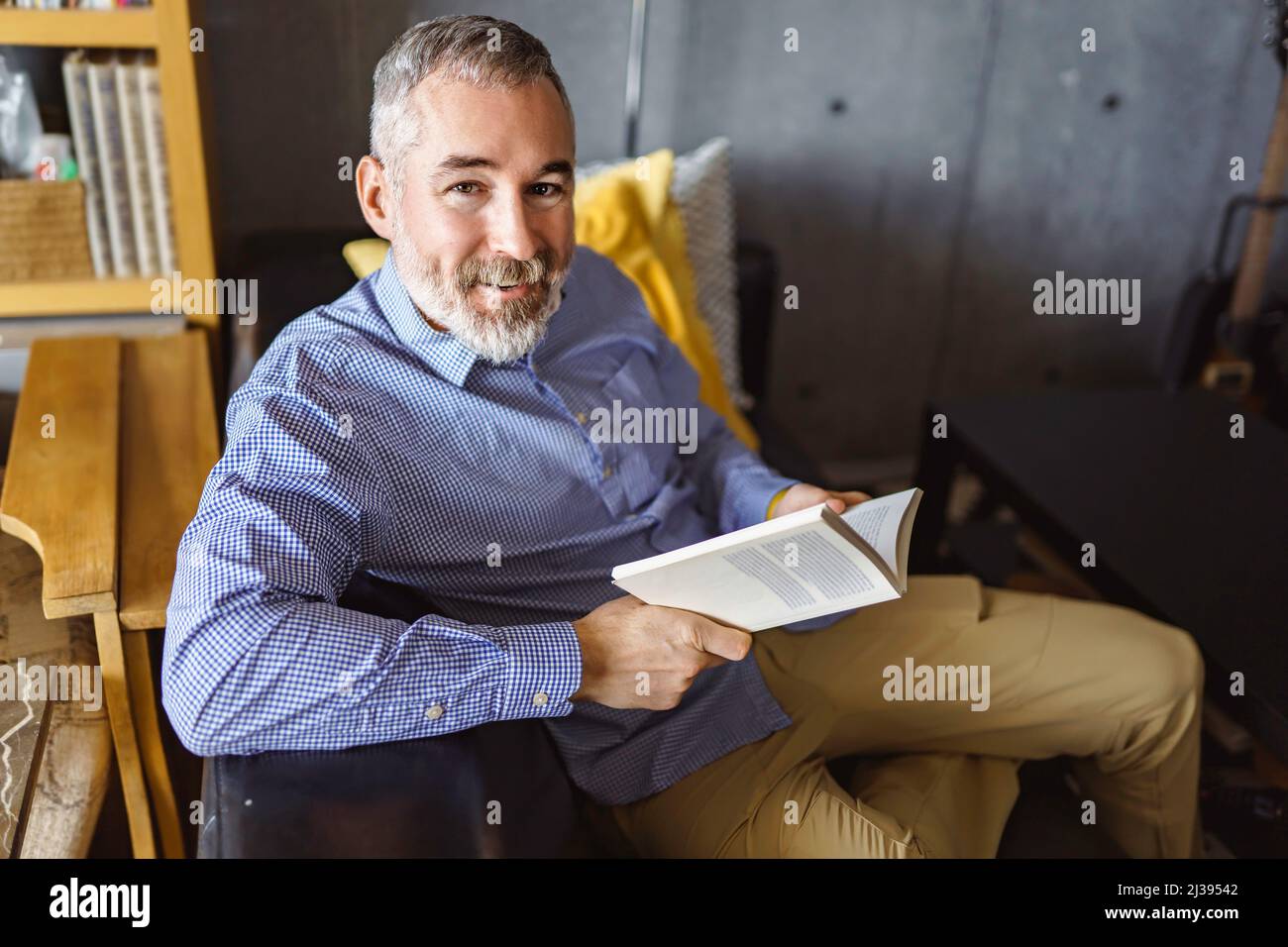 Reifer Mann, der einen Büchersitz liest, sieht aus wie Entspannung Stockfoto