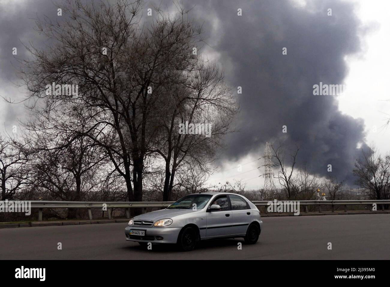 Non Exclusive: ODESA, UKRAINE - 3. APRIL 2022 - Ein Auto bewegt sich entlang einer Autobahn als Rauch aus dem Feuer auf dem Gebiet einer Ölraffinerie und Stockfoto