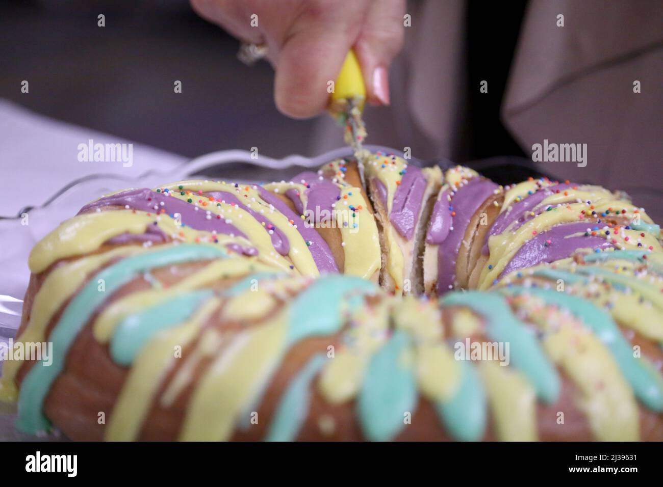 Nahaufnahme einer Frau, die in eine bunte Mardi Gras King Cake schneidet. Stockfoto