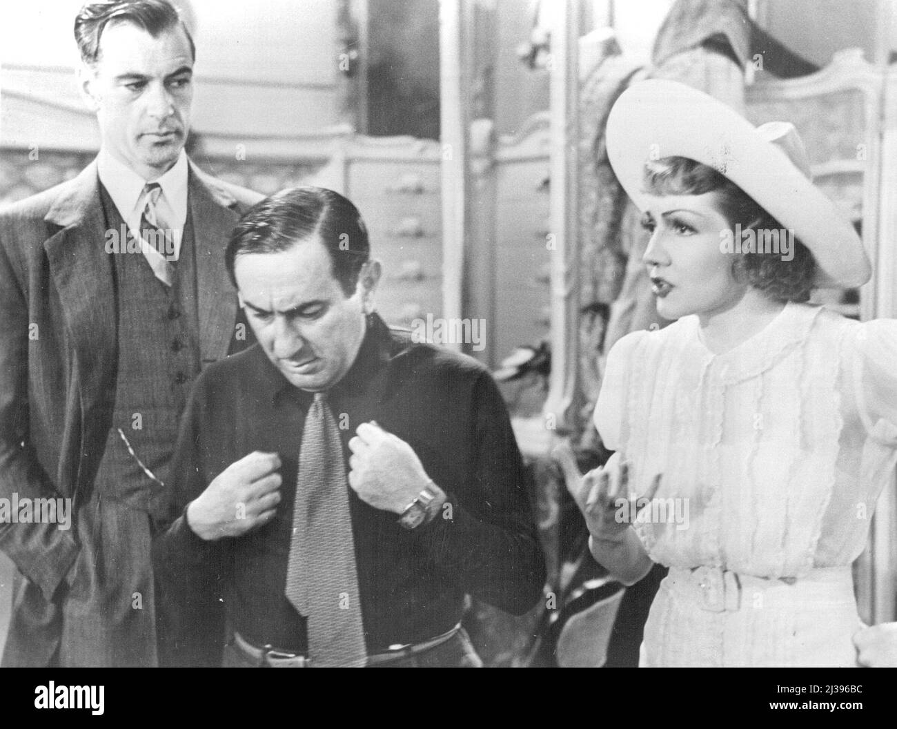 Regisseur bei der Arbeit: Diese Bilder führen Sie hinter die Kulissen von Bluebeards Achte Frau und zeigen Ihnen einige der Geheimnisse des berühmten Lubitsch-Touch. Hier zeigt Ernst Lubitsch, wie Gary Cooper den Morgenmantel anziehen kann - oder vielleicht ist es der Pyjama-Mantel, der eine so große Rolle auf dem Bild spielt. Sie sehen, Gary ist ein Millionär, der in ein Geschäft an der französischen Riviera geht, um Pyjamas zu kaufen und darauf besteht, dass er nur die Oberteile will, und -- jedenfalls zeigen die Bilder Lubitsch bei der Arbeit. Mit ihm sind Gary Cooper, Claudette Colbert und das Drehbuchmädchen, das das Drehbuch für seine Führung hält. April 15, Stockfoto
