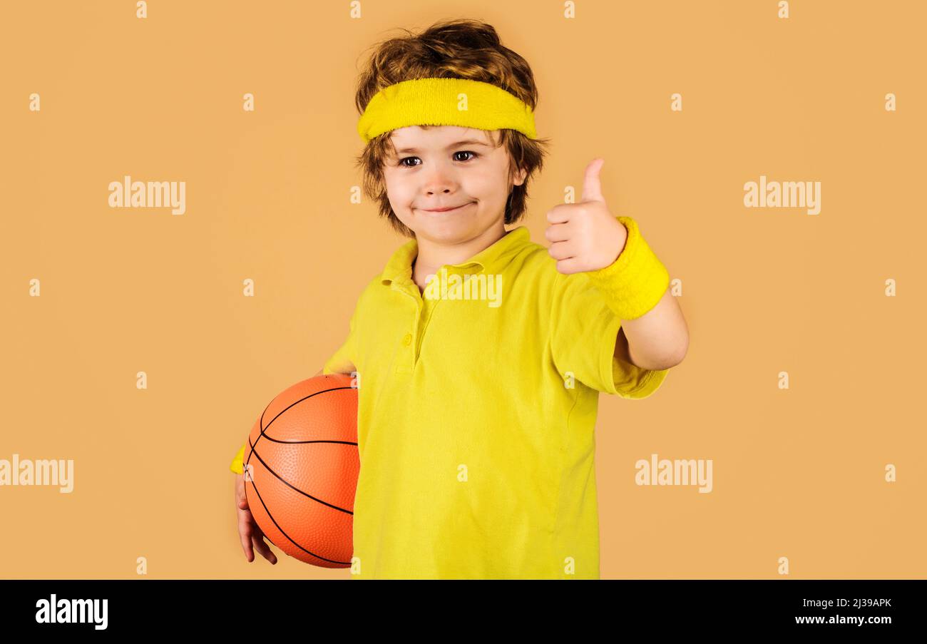 Sportliches Kind mit Basketballball, der den Daumen nach oben zeigt. Kleiner Basketballspieler in Sportbekleidung. Stockfoto