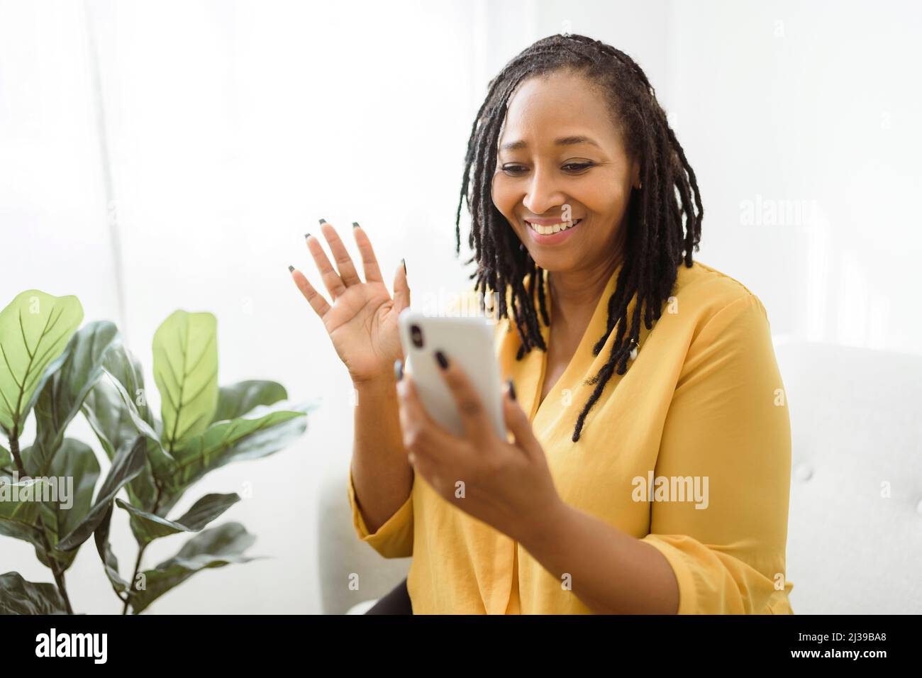 Porträt einer afrikanischen Frau sitzen auf dem Sofa mit Handy sagen hallo Stockfoto