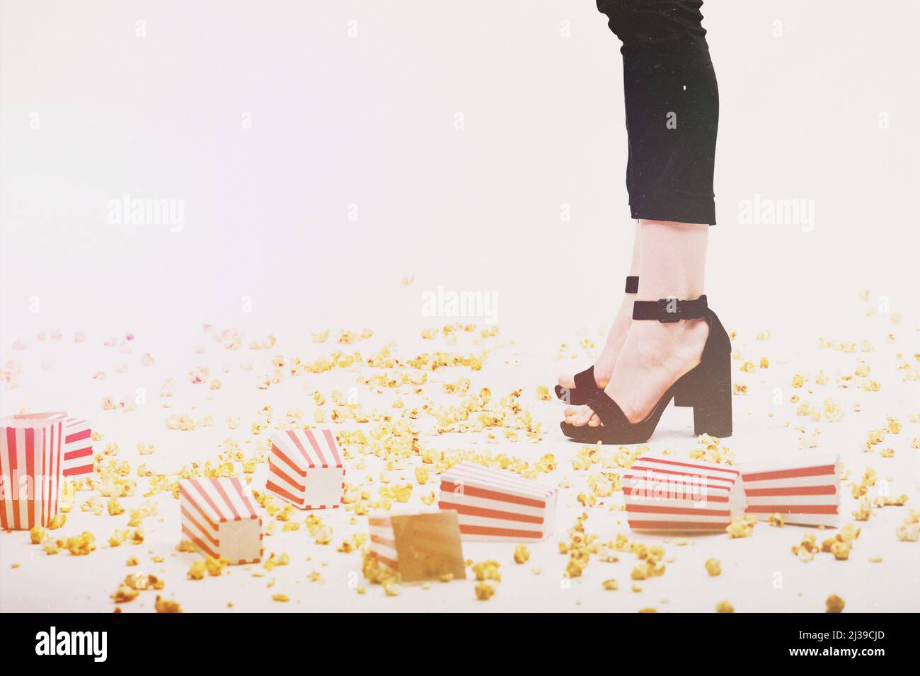 Freizeit- und Lifestyle-Konzept. Viele Popcorn- und Kisten wurden auf den Boden geworfen und Frauenbeine mit schwarzen Hosen und Schuhen mit hohem Absatz auf weißem Hintergrund. Vint Stockfoto