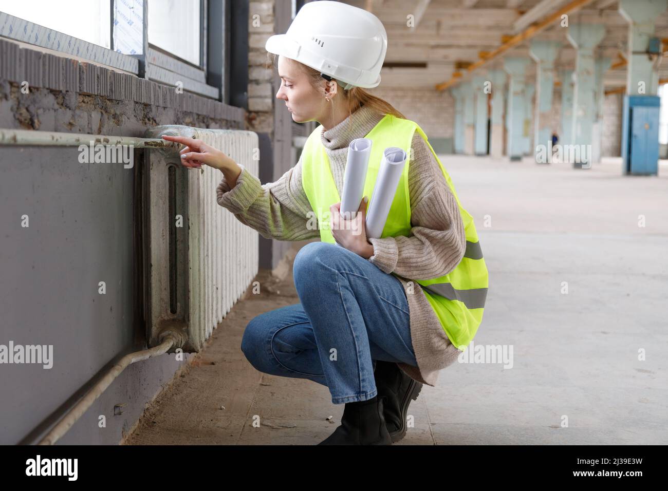 Eine Ingenieurin inspiziert alte Rohre und Heizkörper der Wasserheizung vor dem Wiederaufbau Stockfoto