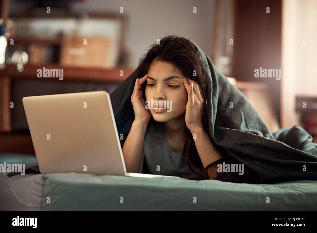 Ich kann gar nicht glauben, was ich lese. Aufnahme einer jungen Frau, die mit Bestürze auf ihren Laptop schaut, während sie im Bett liegt. Stockfoto