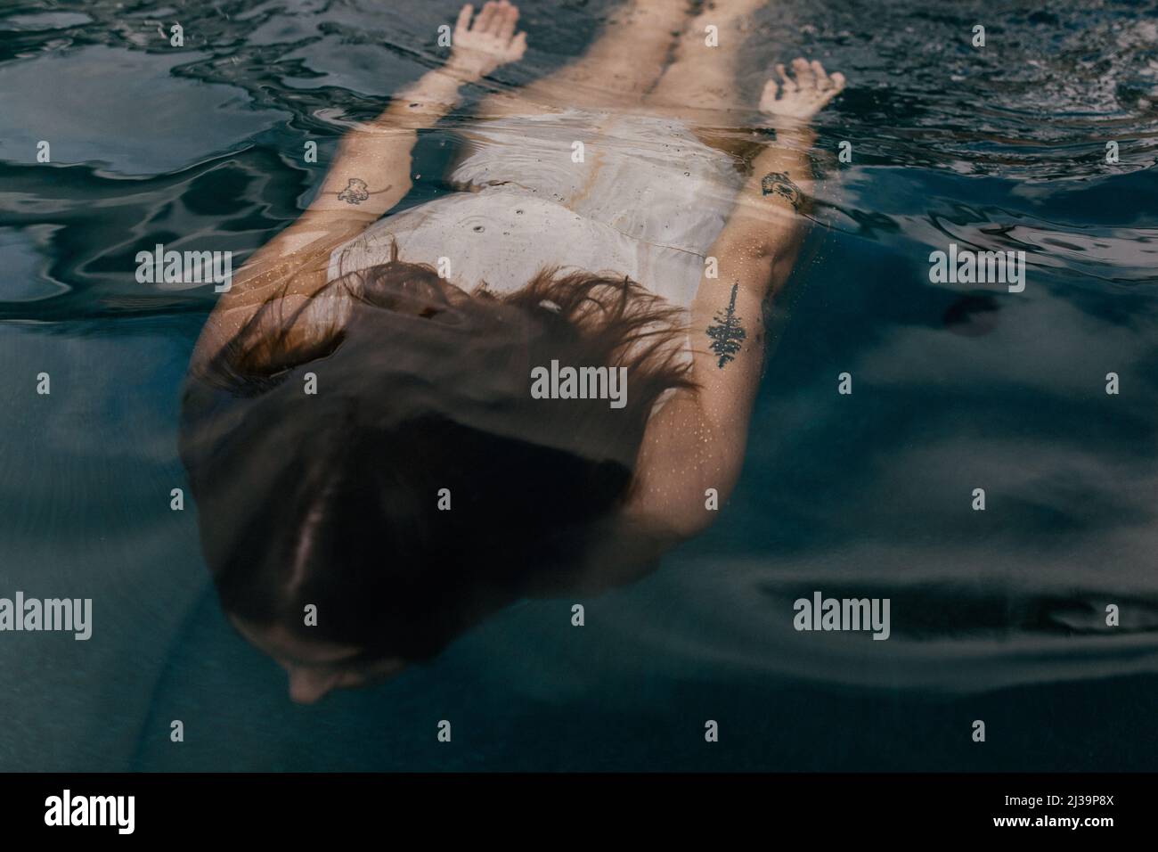 Frau mit Tattoos schwimmend unter Wasser im dunklen Pool Stockfoto