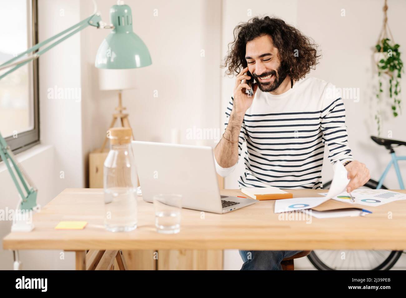 Fröhlicher junger Mann, der während der Arbeit von zu Hause aus telefoniert Stockfoto