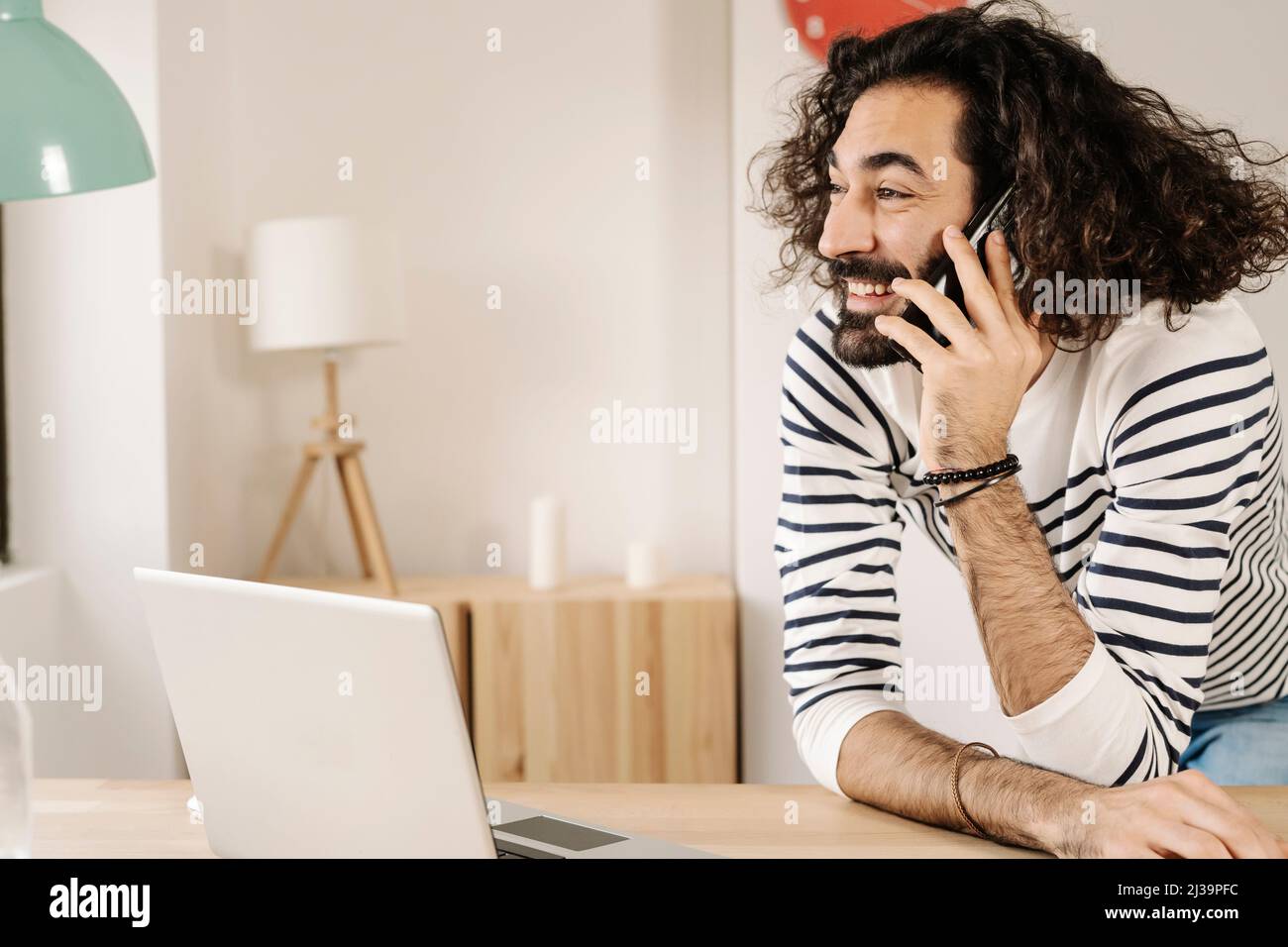 Fröhlicher Mann, der zu Hause mit seinem Laptop telefoniert Stockfoto