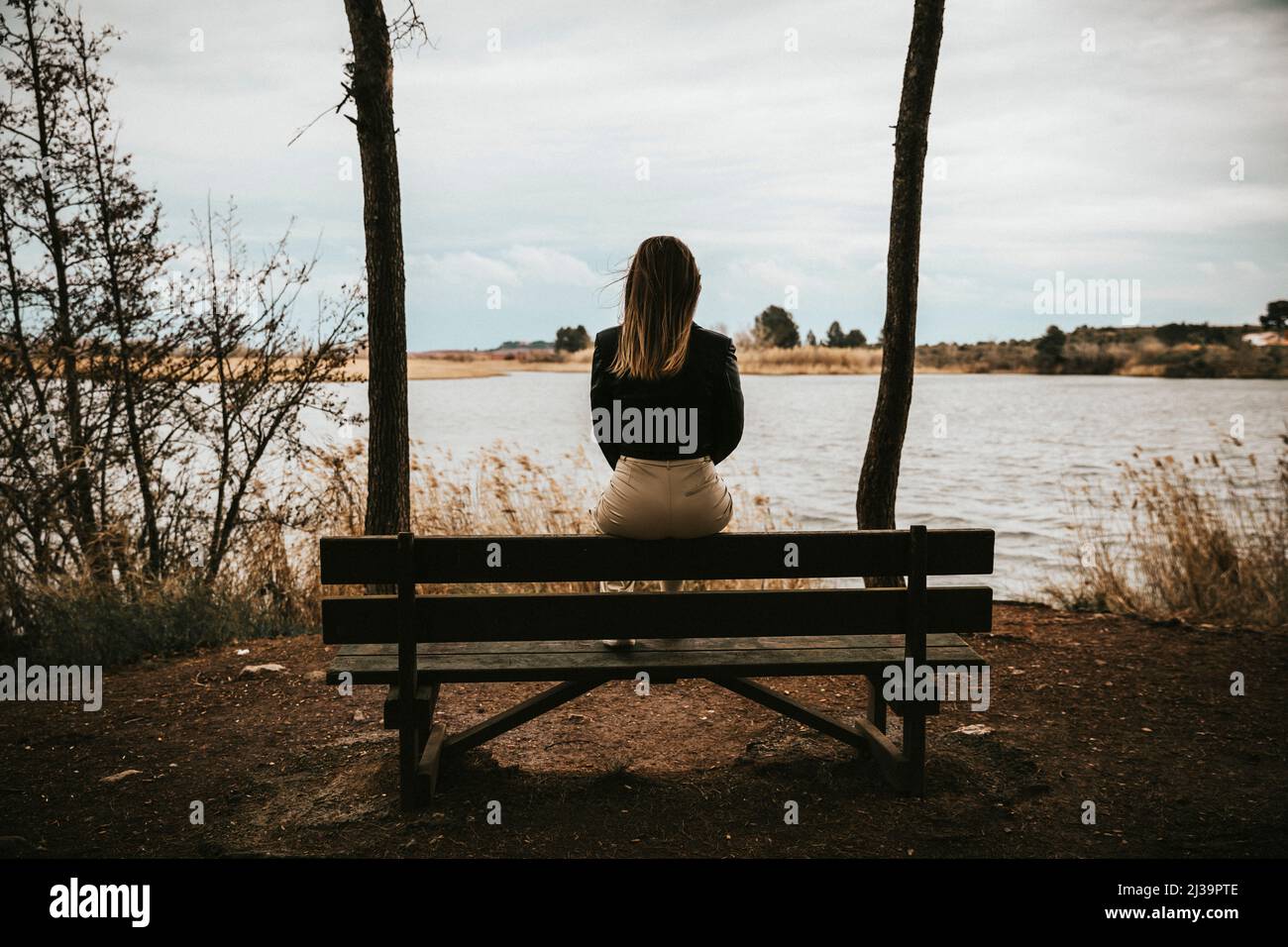 Unkenntlich trauriges Mädchen, das auf einer Bank sitzt, während es auf einen See blickt Stockfoto