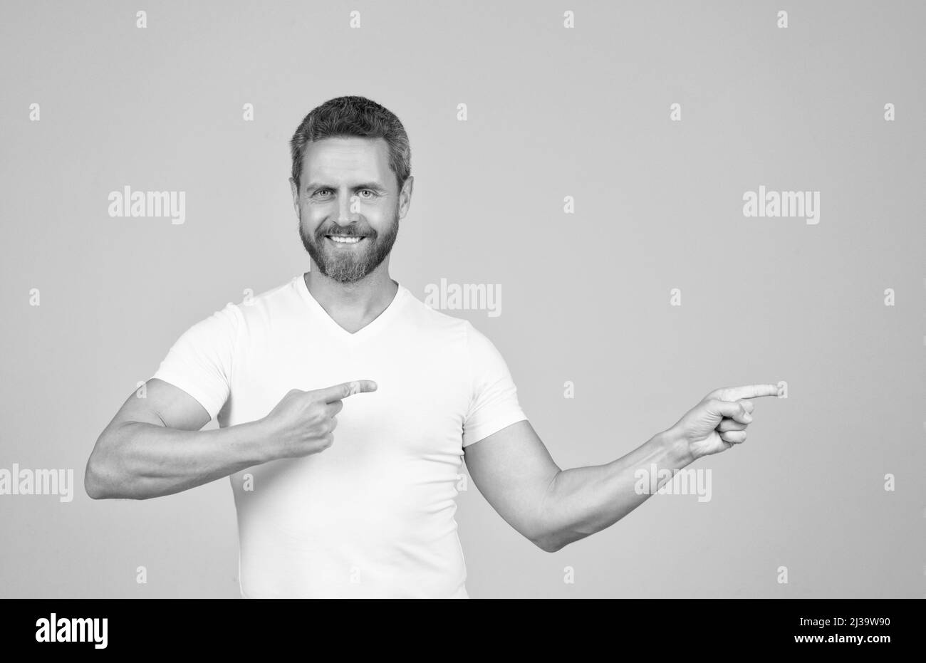 Glücklicher gutaussehender Kerl in weißem T-Shirt Lächeln zeigt Finger beiseite Werbegeste, Werbung Stockfoto