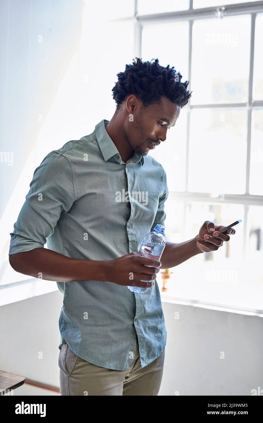 Senden eines Kurztextes. Ausgeschnittene Aufnahme eines jungen Designers, der in einem Büro auf seinem Handy SMS schreibt. Stockfoto